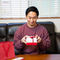バレンタインに女性社員からもらったプレゼントを開封する男性の笑顔の写真