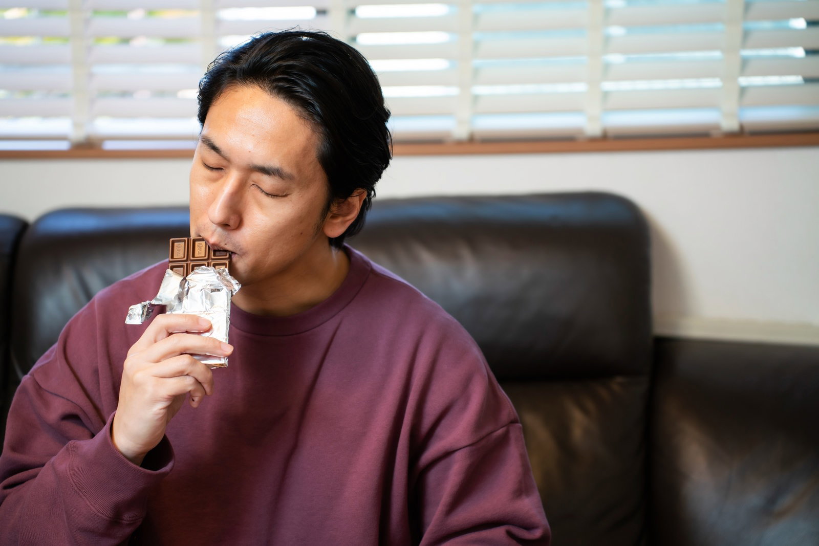 紫色のシャツを着た男性が板チョコを手に持ち食べている［モデル：大川竜弥］
