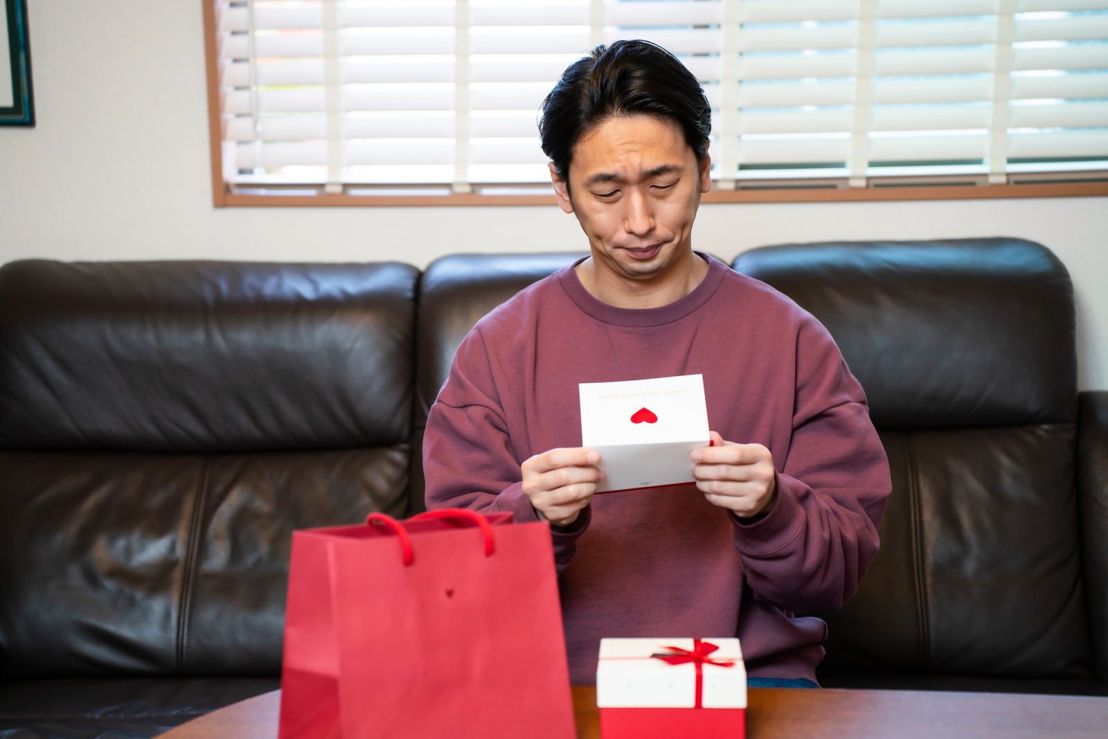 ソファに座って手紙を読む男性と赤いプレゼント袋［モデル：大川竜弥］