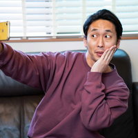 顔に手を添えて小顔アピールする自撮り男子の写真