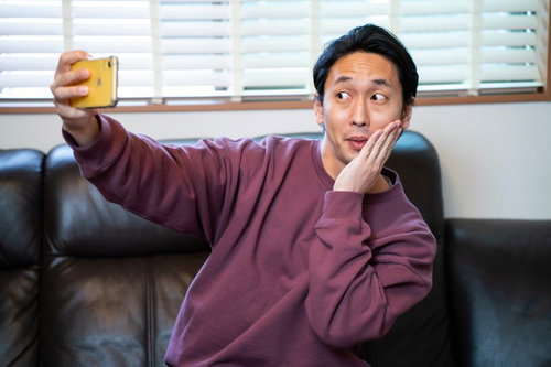 顔に手を添えて小顔アピールする自撮り男子