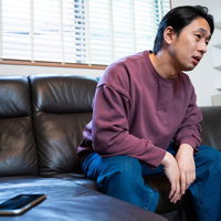 スマホの通知を見て落ち込む男性、ソファで孤独感を感じるの写真