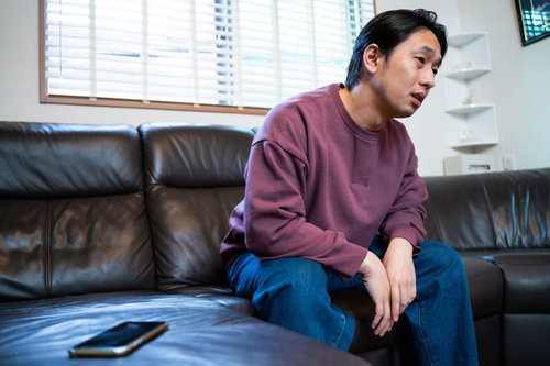 スマホの通知を見て落ち込む男性、ソファで孤独感を感じる