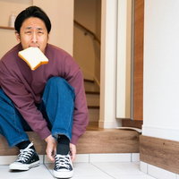 遅刻しそうで食パンを咥えながらスニーカーを履く男性の写真