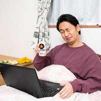 ベッドに入りながらリモート飲みするビール片手の男性の写真