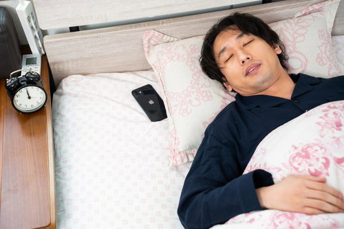 朝寝坊で遅刻する男性がアラームが鳴っているのに爆睡している