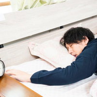 アラームを止めた後、ベッドで二度寝する男性の写真