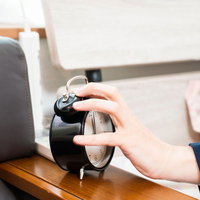 朝の寝坊防止、目覚まし時計のベルを止める男性の写真