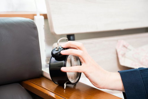 朝の寝坊防止、目覚まし時計のベルを止める男性