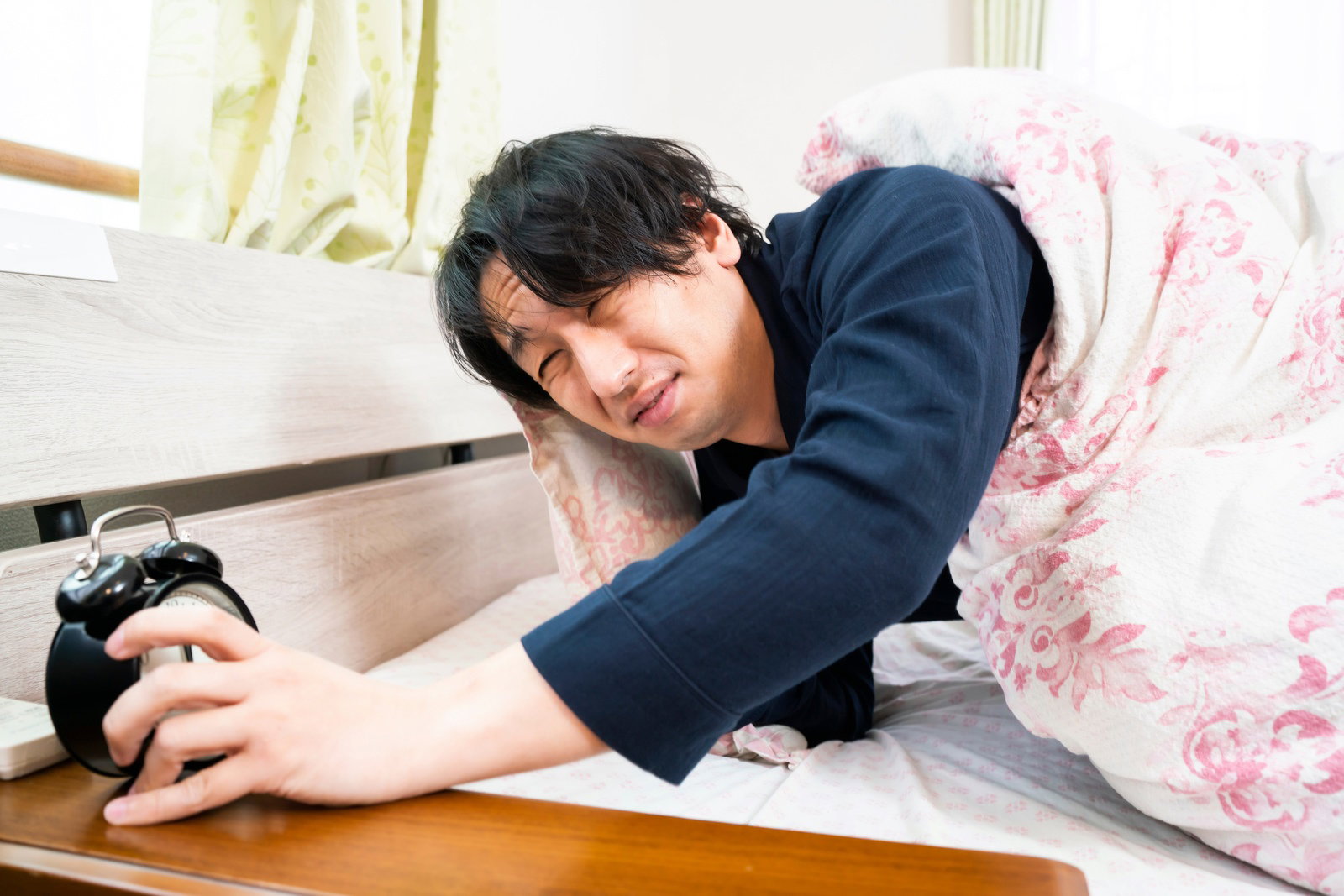 ベッドで目覚まし時計のアラームを止めようとする男性