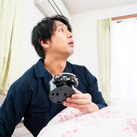 目覚まし時計が鳴らず昼過ぎに起きてしまった男性の写真