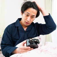 飛び起きるがすでに時おすし、目覚まし時計を見て慌てる男性の写真