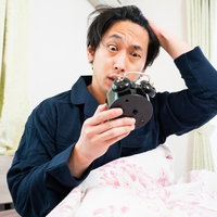 アラームをセットし忘れて寝坊し慌てる男性の写真