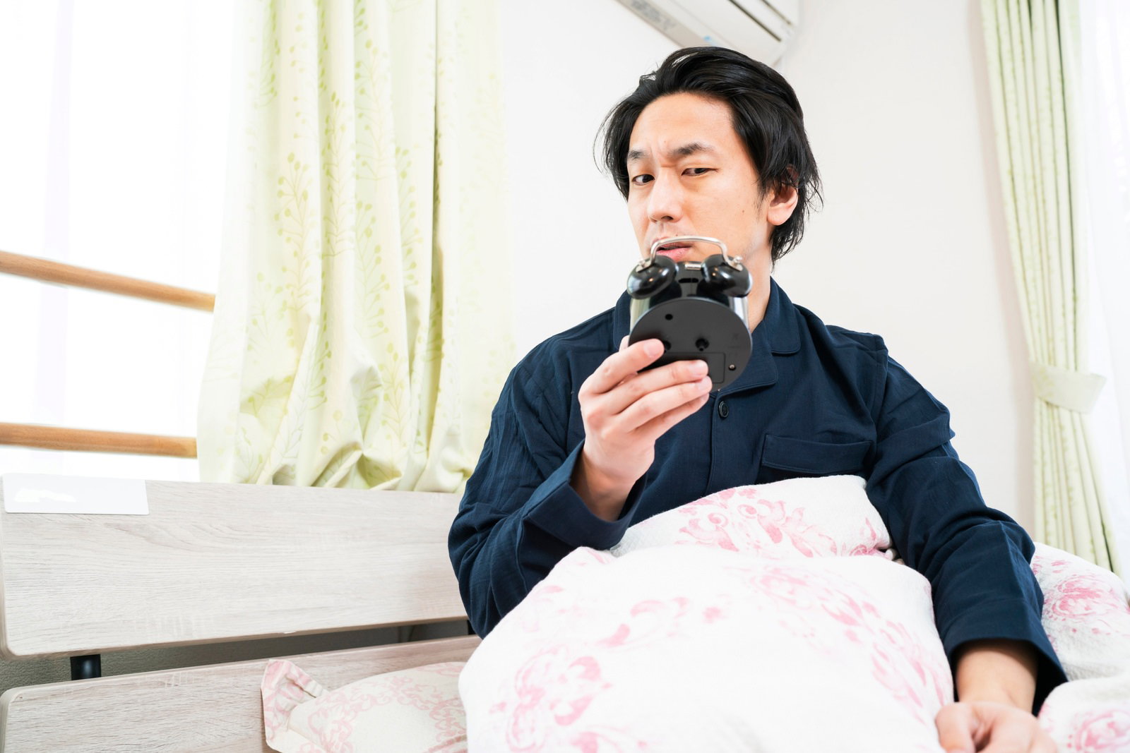 白い布団の中でスマートフォンを見つめる男性［モデル：大川竜弥］