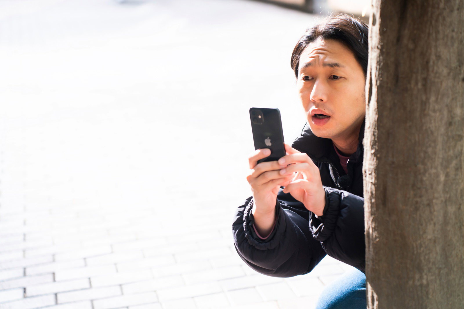 壁の陰から身を隠しながらスマートフォンで撮影する男性［モデル：大川竜弥］