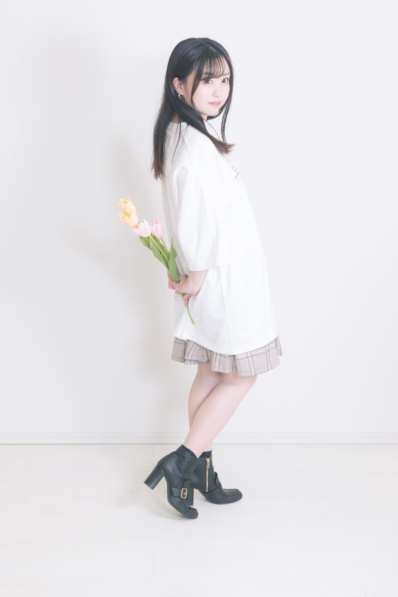 白いTシャツとチェックスカート、黒いブーツを着た女性がチューリップを手に持ち振り返っている［モデル：河村友歌］