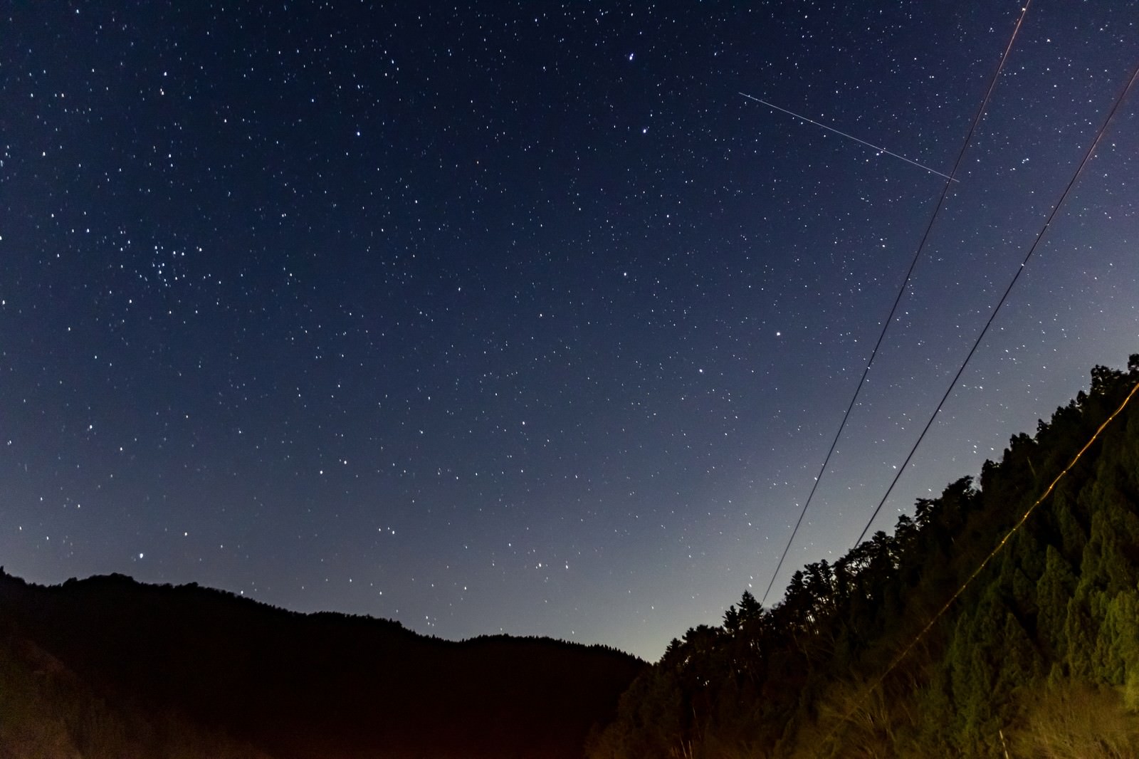 無数の星が輝く夜空に流れ星が光り山のシルエットが見える風景
