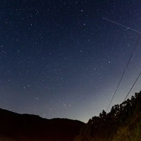 流れ星と雲ひとつない夜空に映る山のシルエットの写真