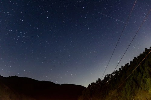 流れ星と雲ひとつない夜空に映る山のシルエット