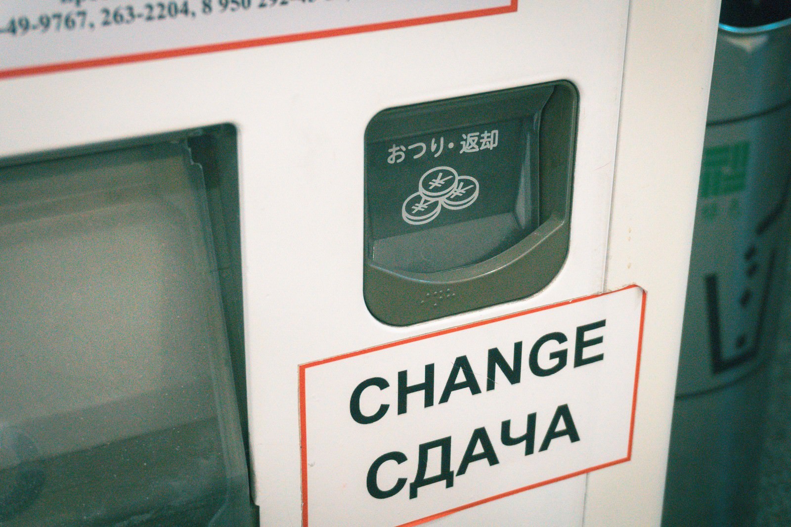 ロシアで稼働する日本製自動販売機のおつり返却ボタン。緑色のボタンに日本語と多言語表記