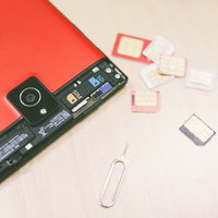 赤いスマートフォンとSIMカード、ピンのセットの写真