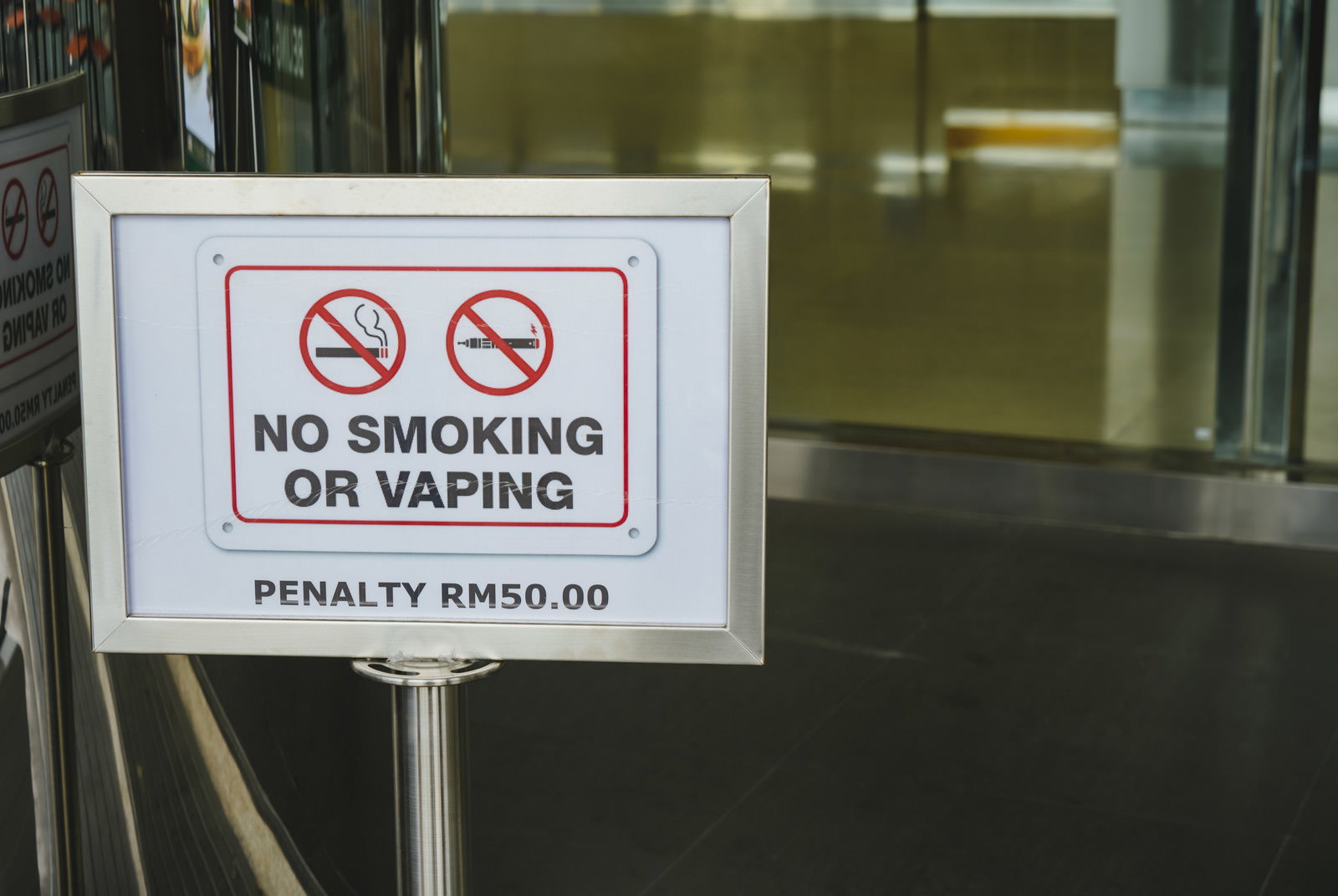 白い枠の看板に赤い禁止マーク2つと「NO SMOKING OR VAPING」の表記、罰金額表示