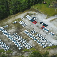 広い駐車場に整然と止まる白い車や多数の車両の写真