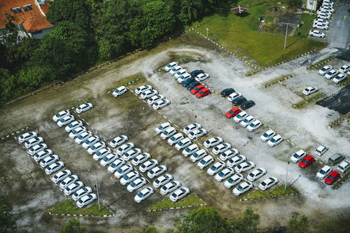 広い駐車場に整然と止まる白い車や多数の車両