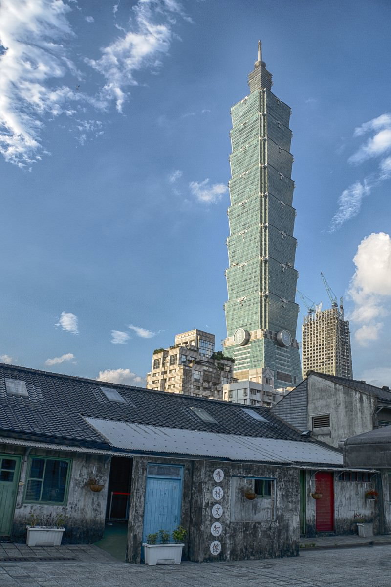 古い町家の背後にそびえる台北101の高層ビル