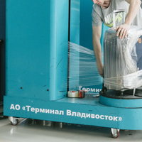 空港で青いラッピング機械を使ってキャリーバッグをフィルムでぐるぐる巻きの写真