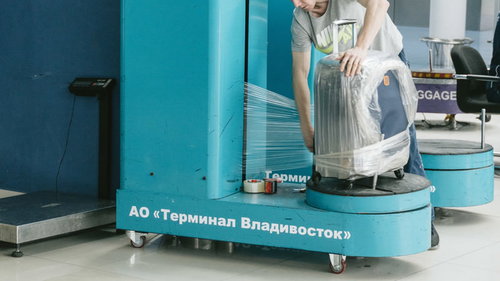 空港で青いラッピング機械を使ってキャリーバッグをフィルムでぐるぐる巻き