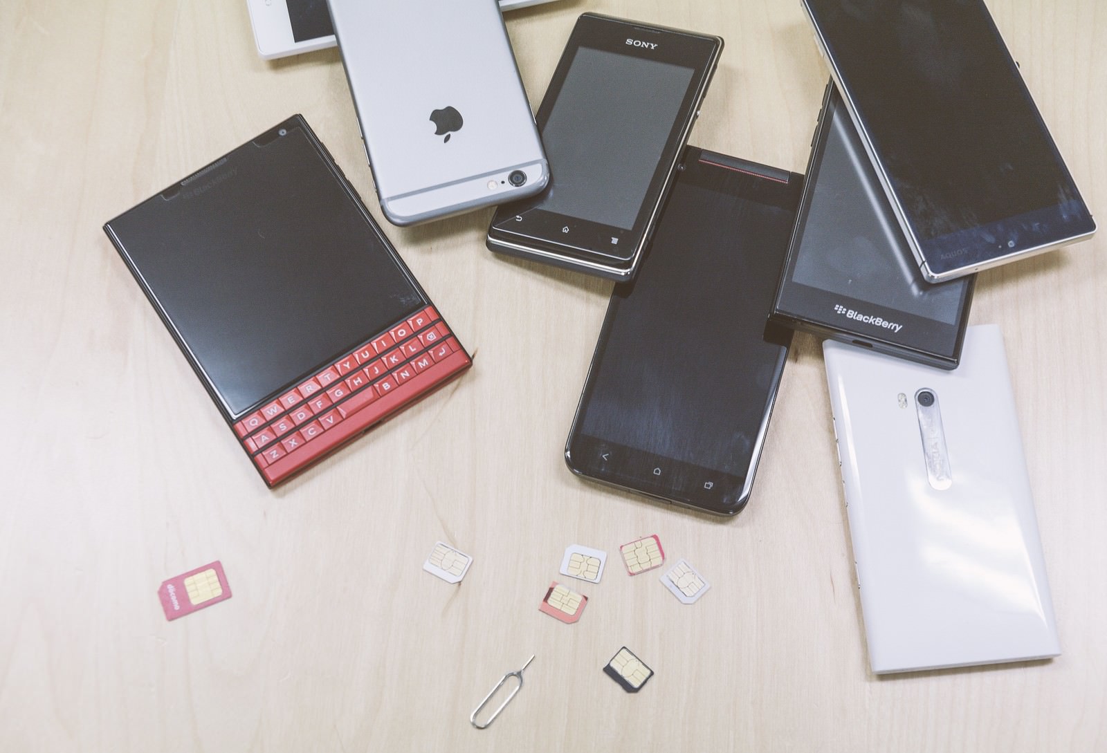 テーブルに散らばった複数台のスマートフォンとSIMカード