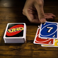 UNOで手札から1枚のカードを出す瞬間の木製テーブルでのゲーム風景の写真