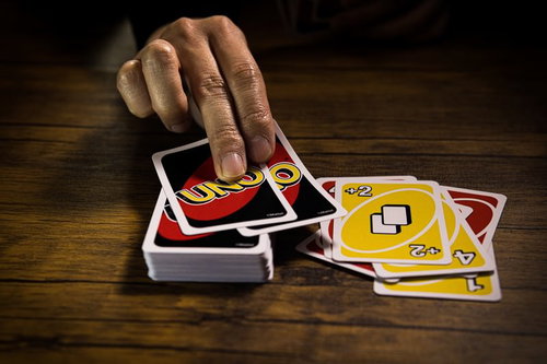 木製テーブルでUNOの山札からドロー2カードを引く