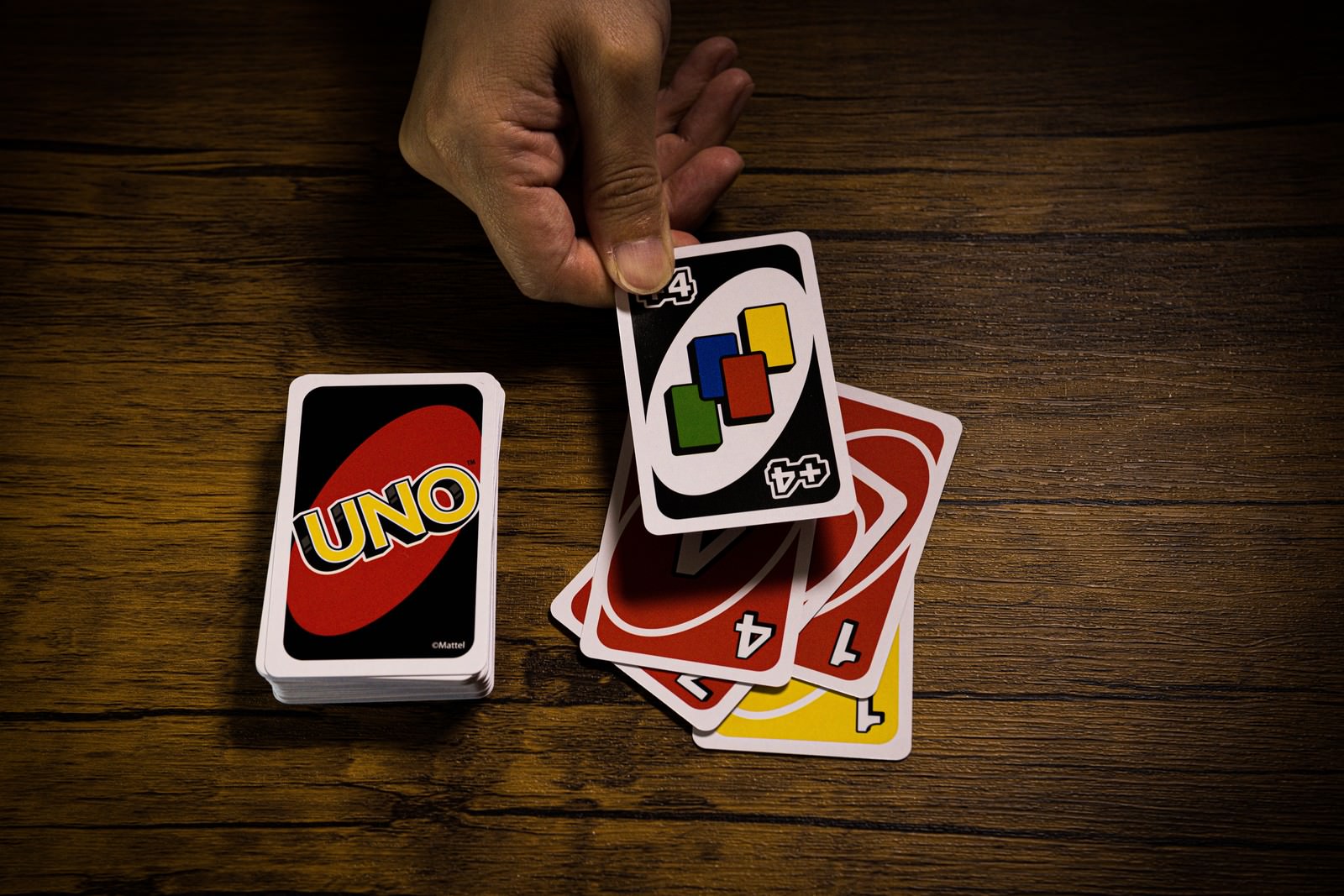 木製テーブル上でUNOのワイルド ドロー4カードを出す手
