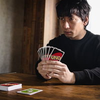 対戦相手の表情を読み取るプレイヤー、ウノで真剣勝負に臨む男性の写真