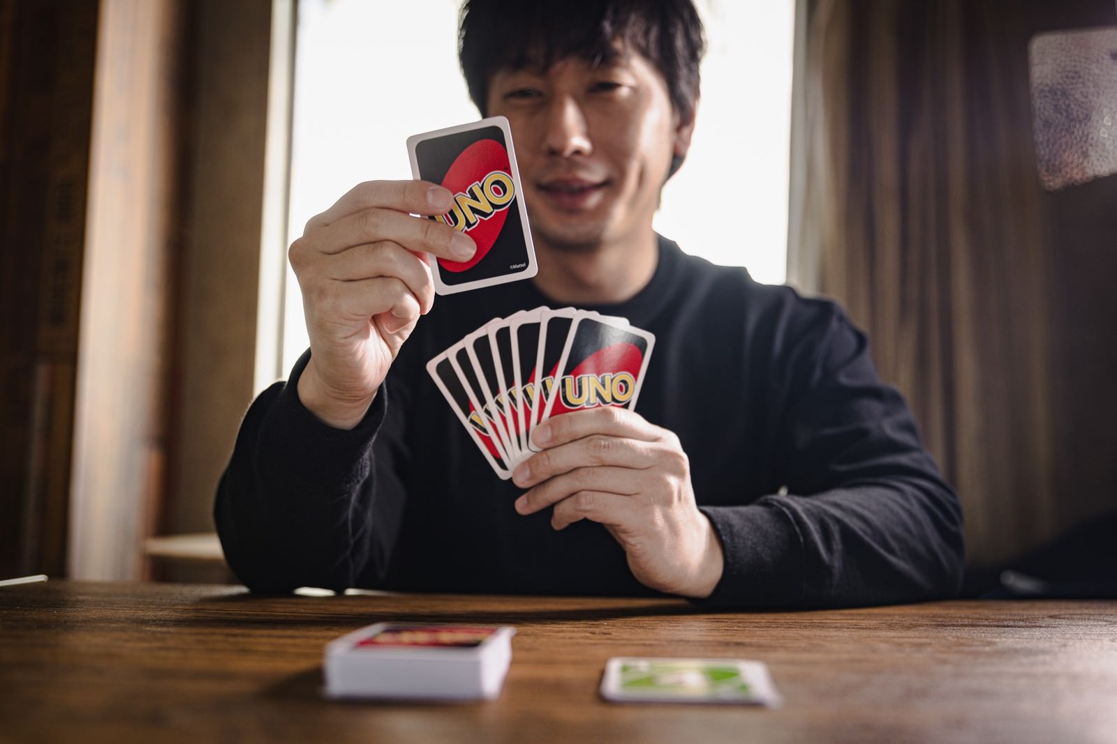 UNOのカードを手に持って嬉しそうに笑顔を見せる男性［モデル：大川竜弥］