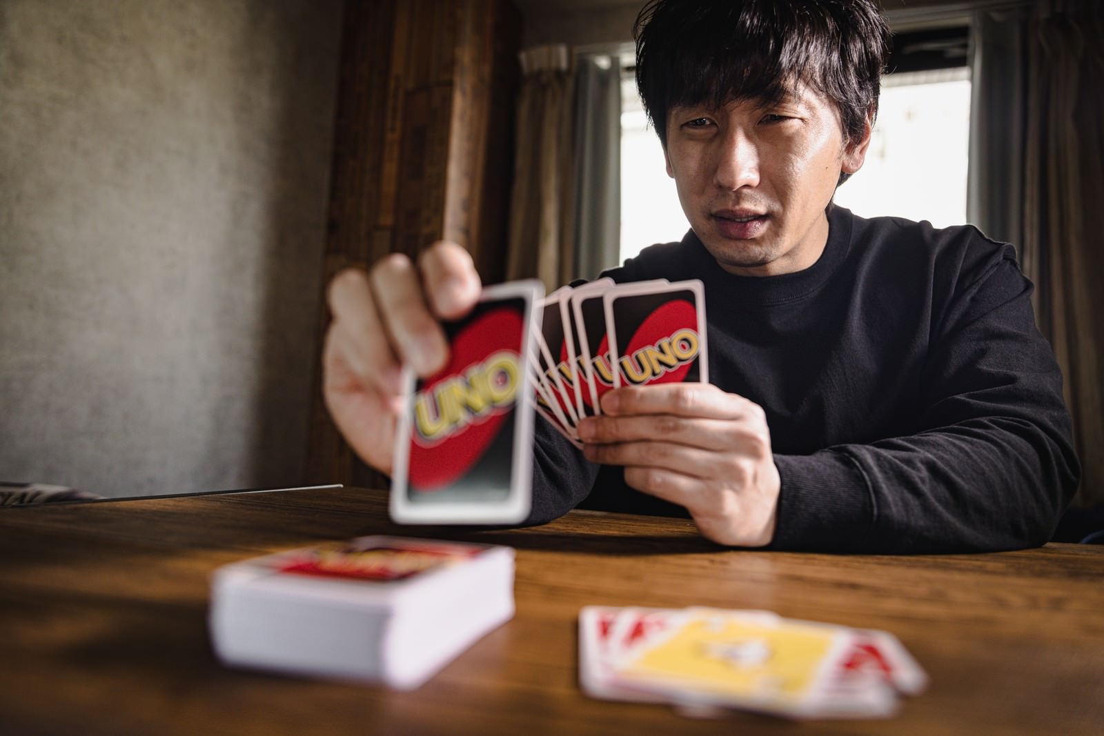 室内でウノのカードを手に持ってゲームをする男性［モデル：大川竜弥］