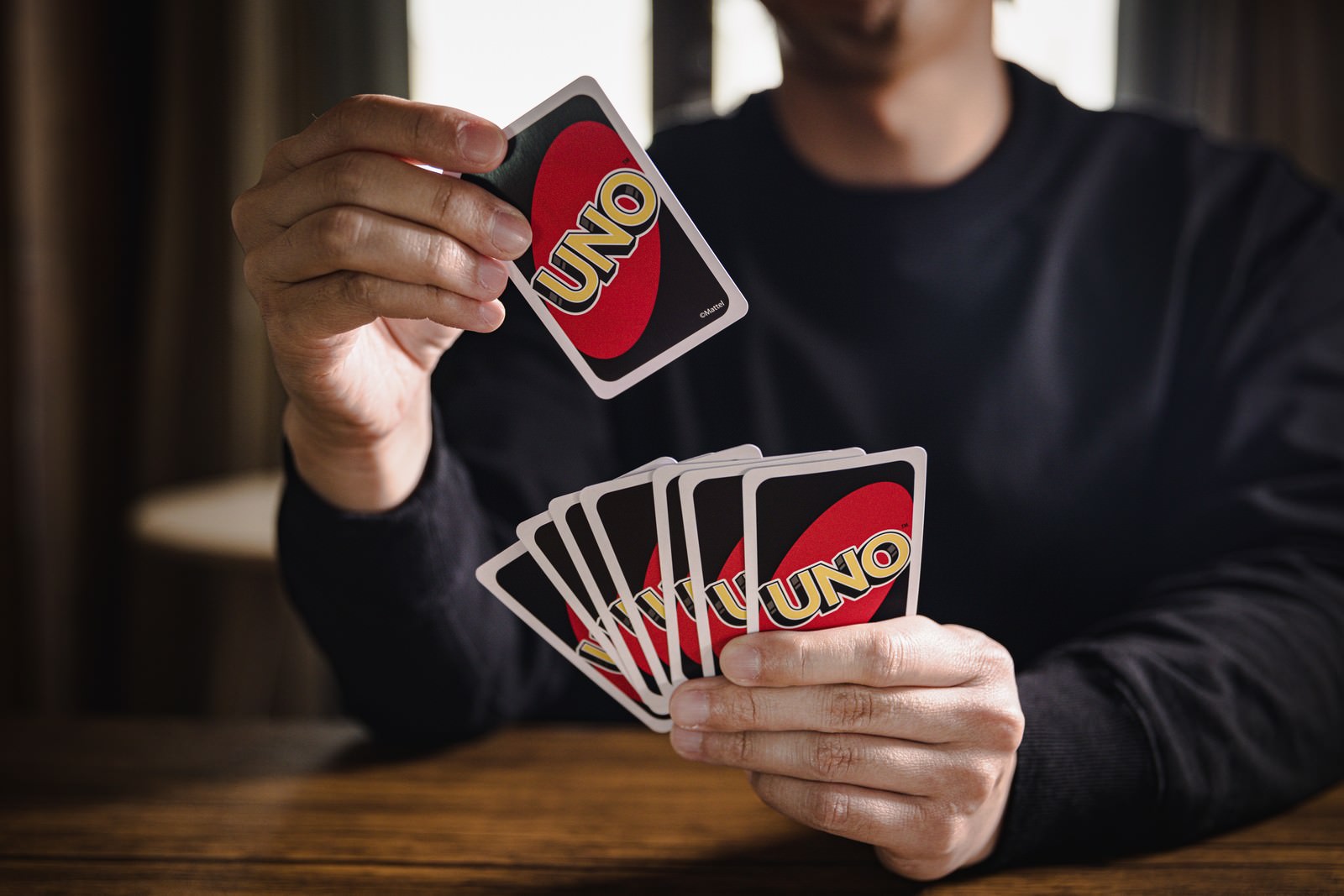 UNOのカードを手に持ち、赤いカードを選んでいるプレイヤー［モデル：大川竜弥］