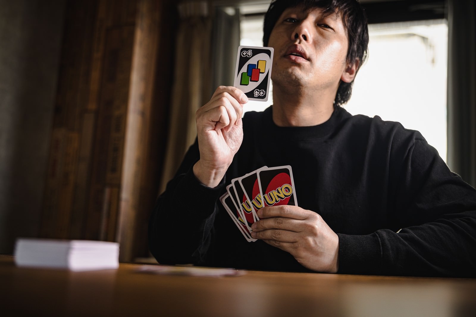 UNOのドロー4カードを出して得意げな表情の男性プレイヤー［モデル：大川竜弥］