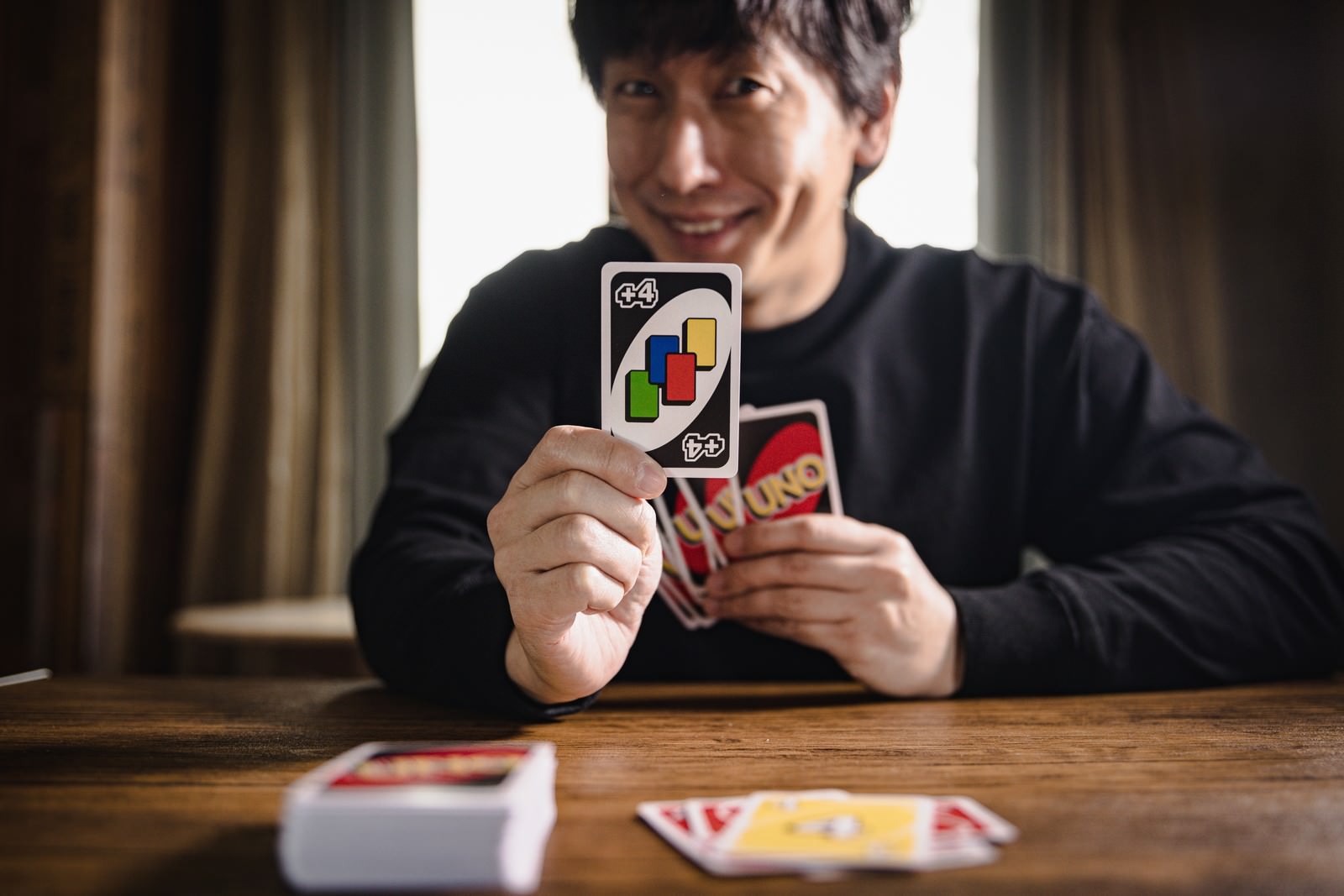 カードゲームで仕返しに成功してニヤリと微笑む黒いスーツの男性［モデル：大川竜弥］