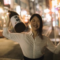 夜の繁華街で酒瓶を掲げて笑う酔っぱらいの女性の写真