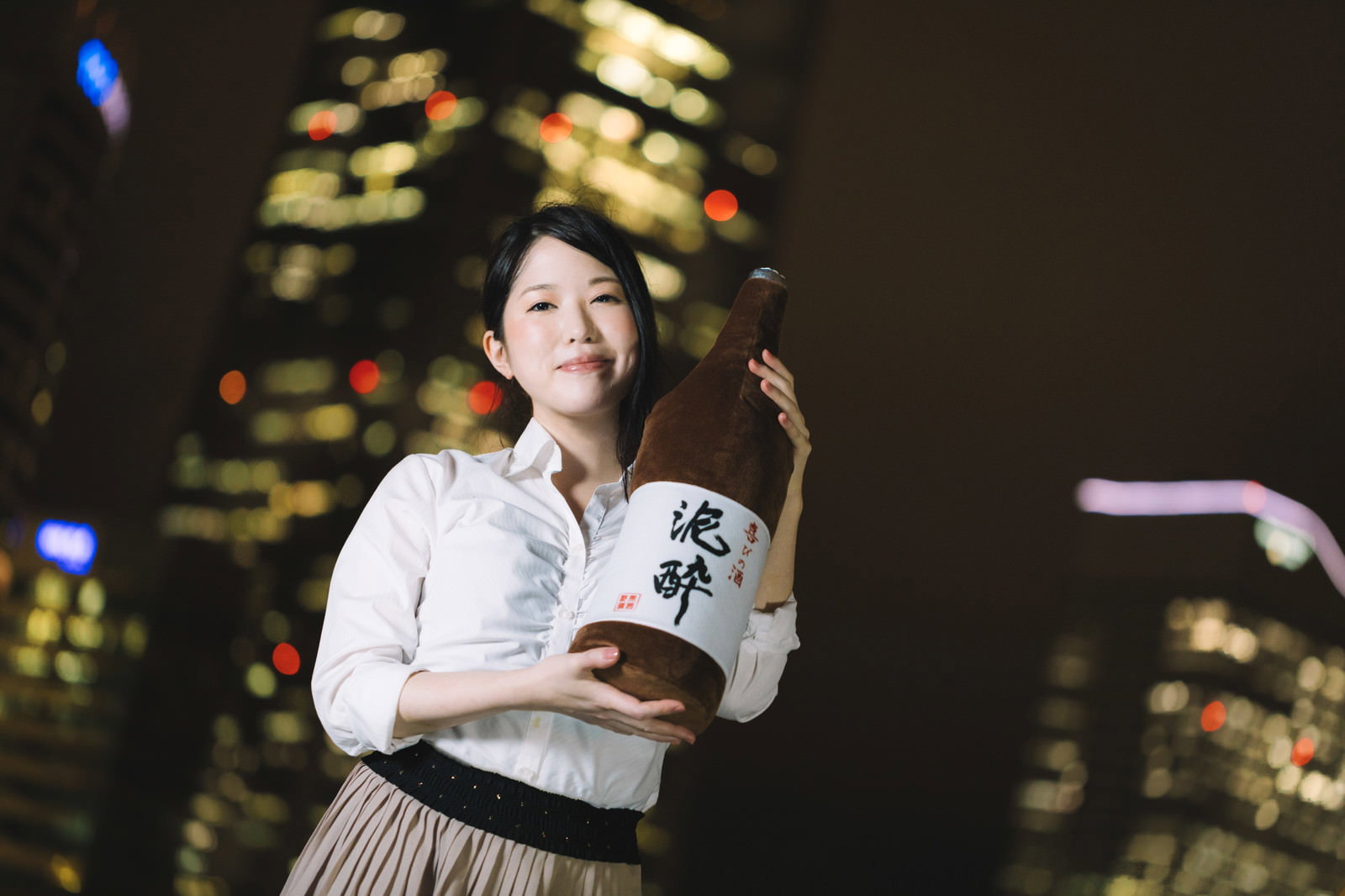 夜景を背景に一升瓶を両手で抱える女性［モデル：シマヅ］