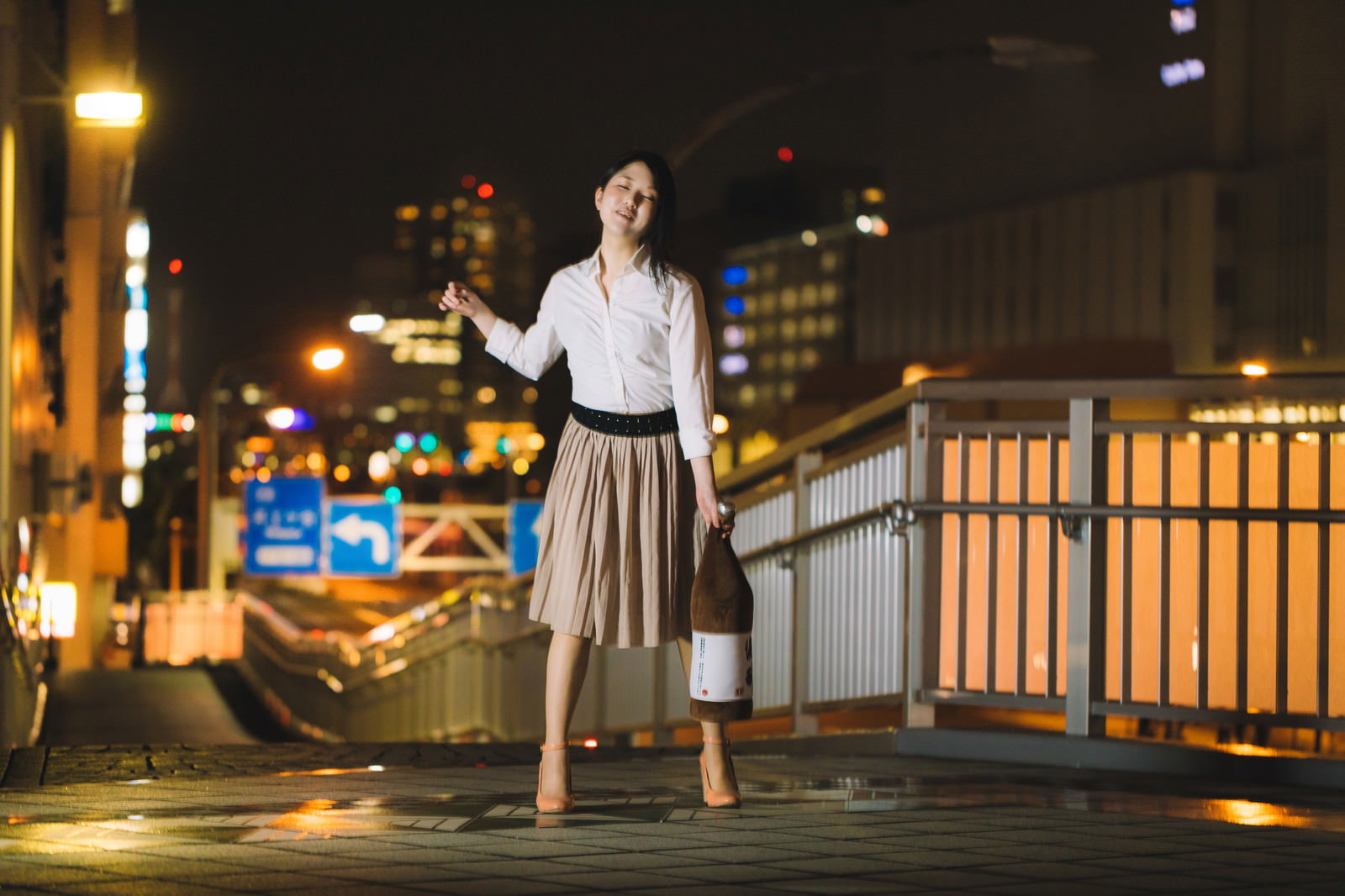 夜間の橋の上で上を向き右手を広げる、白いシャツを着た女性の全身［モデル：シマヅ］