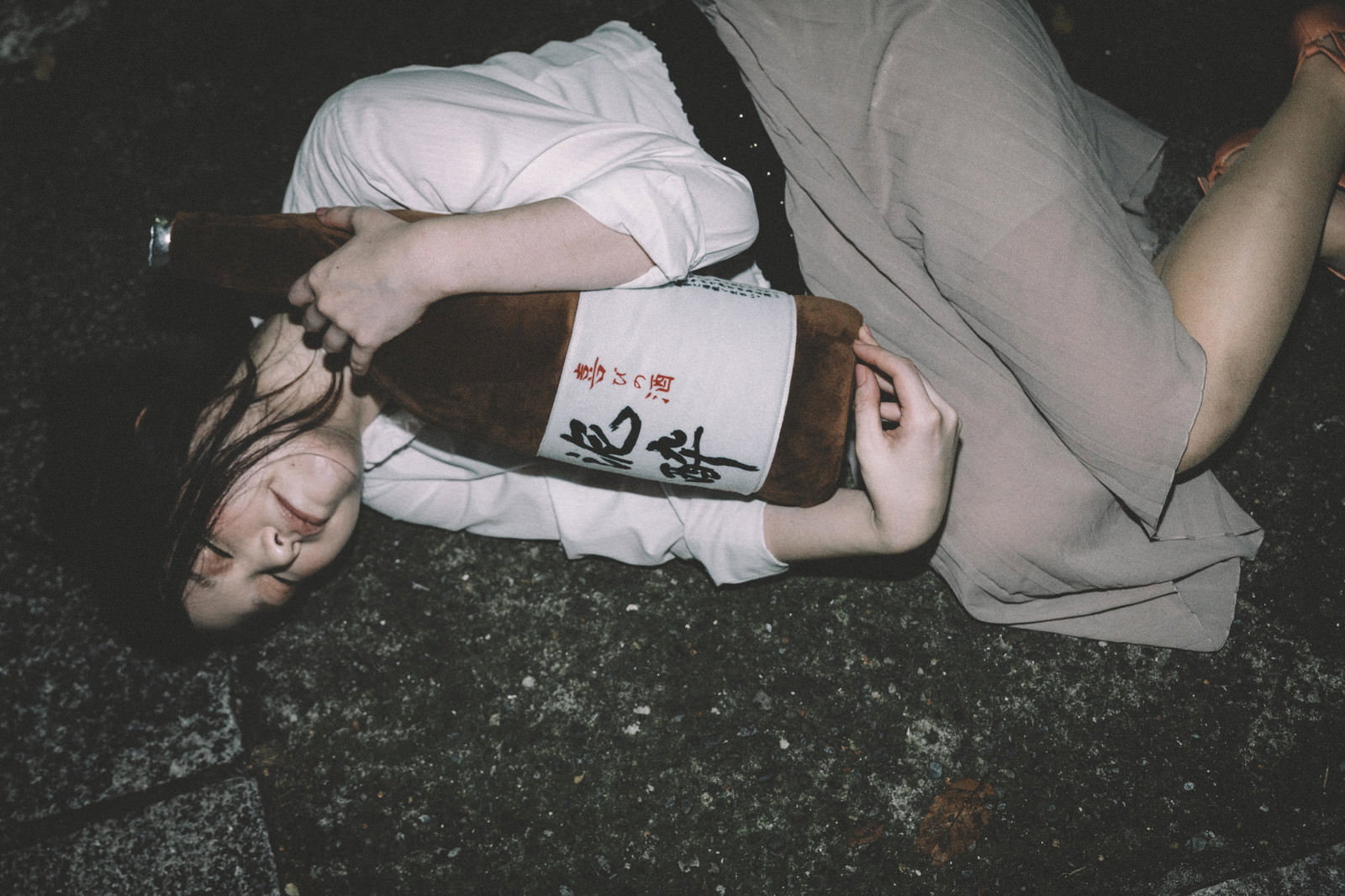 路上で泥酔して横たわり、一升瓶を抱える女性と隣に座る人物［モデル：シマヅ］