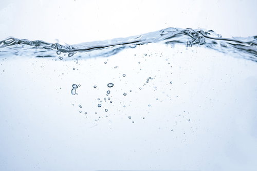 ミネラルウォーターの水面に広がる波と気泡の断面