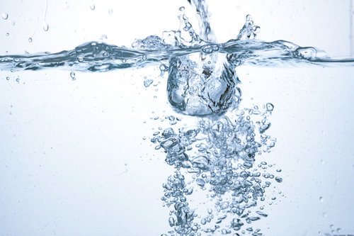 注がれた水としぶき、水中に舞う気泡と氷、ミネラルウォーター