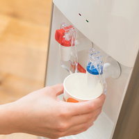 ウォーターサーバーから冷たい水を白いコップに注ぐ手の写真