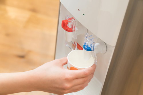 ウォーターサーバーから冷たい水を白いコップに注ぐ手