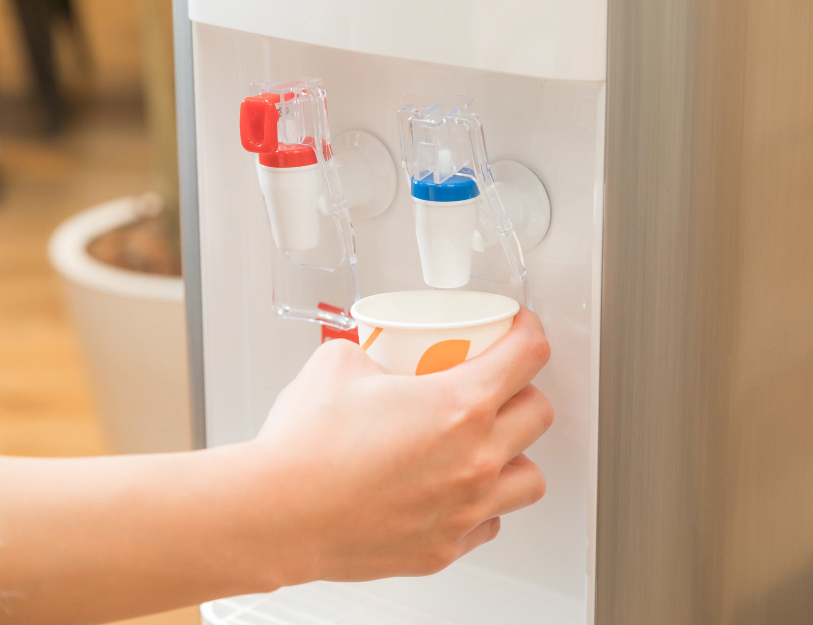 ウォーターサーバーから白い紙コップに冷たい水を注ぐ手